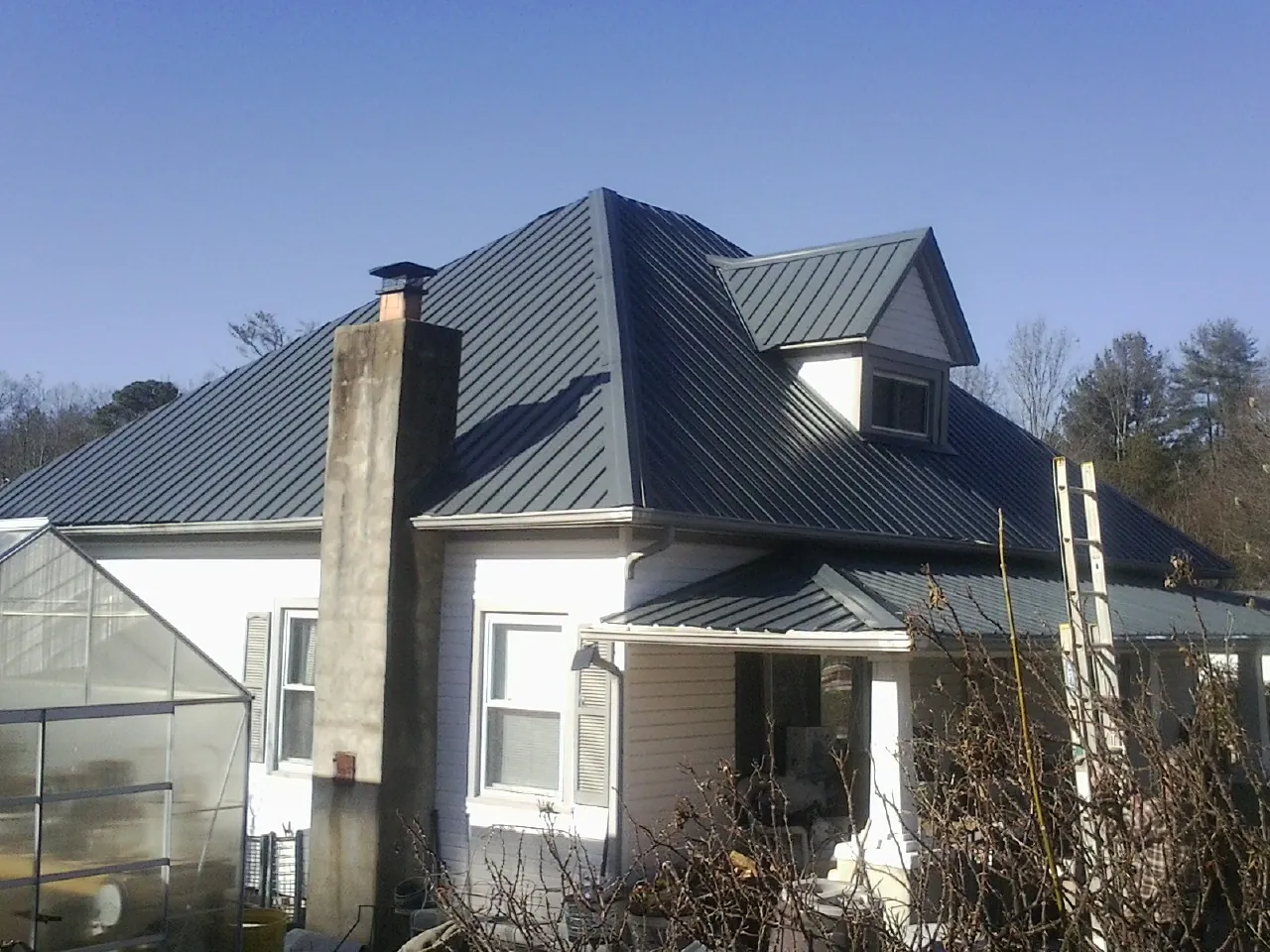 Dark blue standing seam metal roof on a white farmhouse with dormer — Slate & Tile Roof Repair by Roofing Brothers in Farmington
