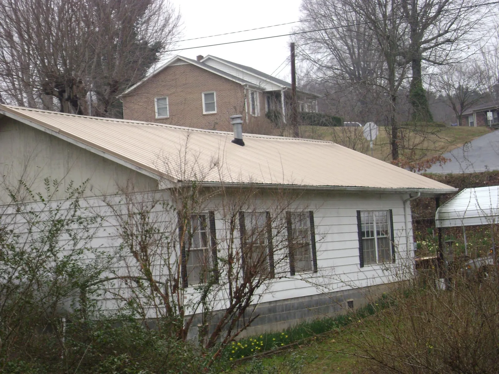 Tan metal roof on a white sided house set into a hillside — Commercial Roofing by Roofing Brothers in Farmington